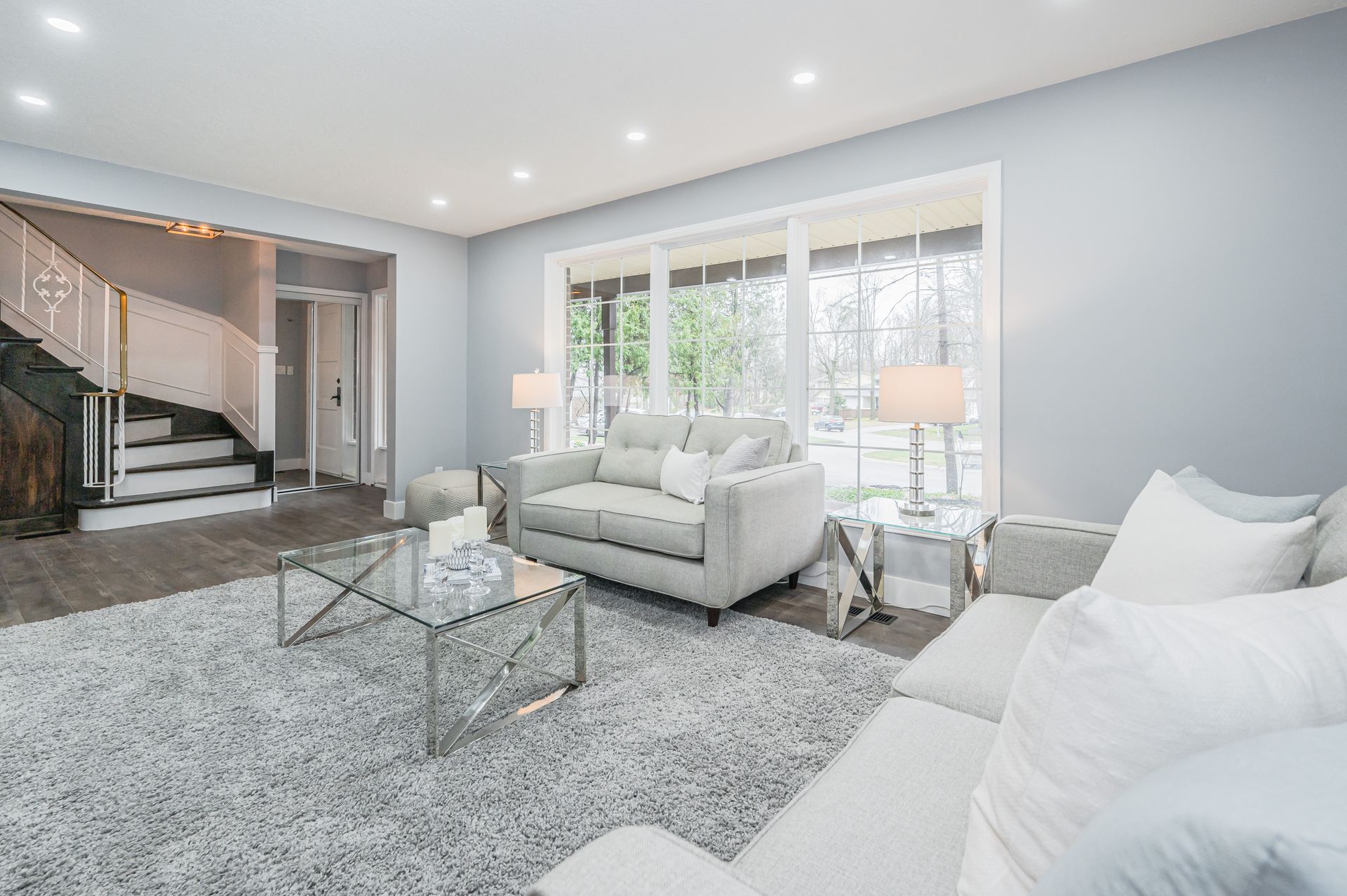 Living room with gray furniture, large window, and staircase, in a house.
