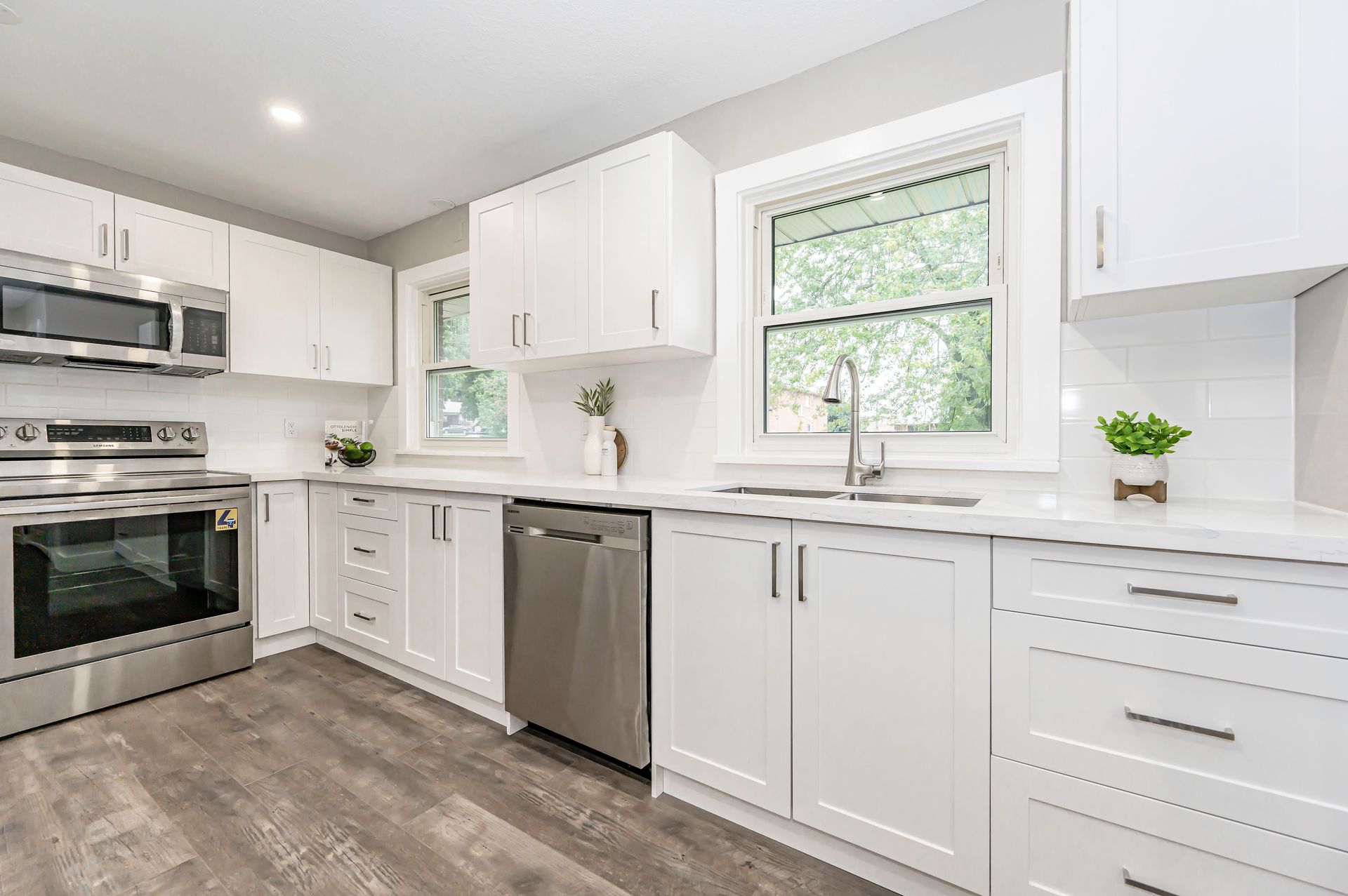 Modern white kitchen with stainless steel appliances, grey flooring, and a window.