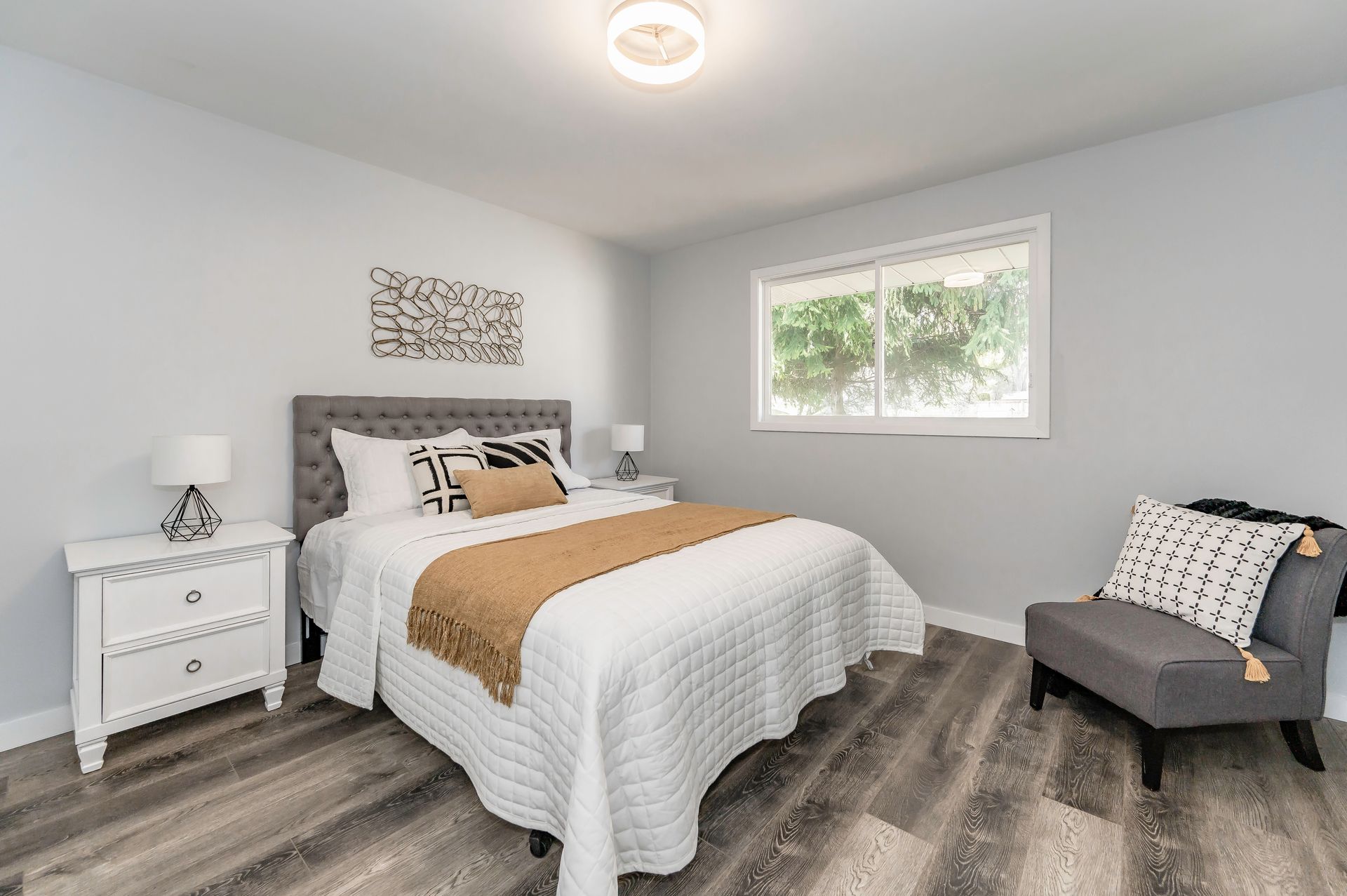 Bedroom with bed, nightstands, chair, and window; gray walls, wood-look floor.