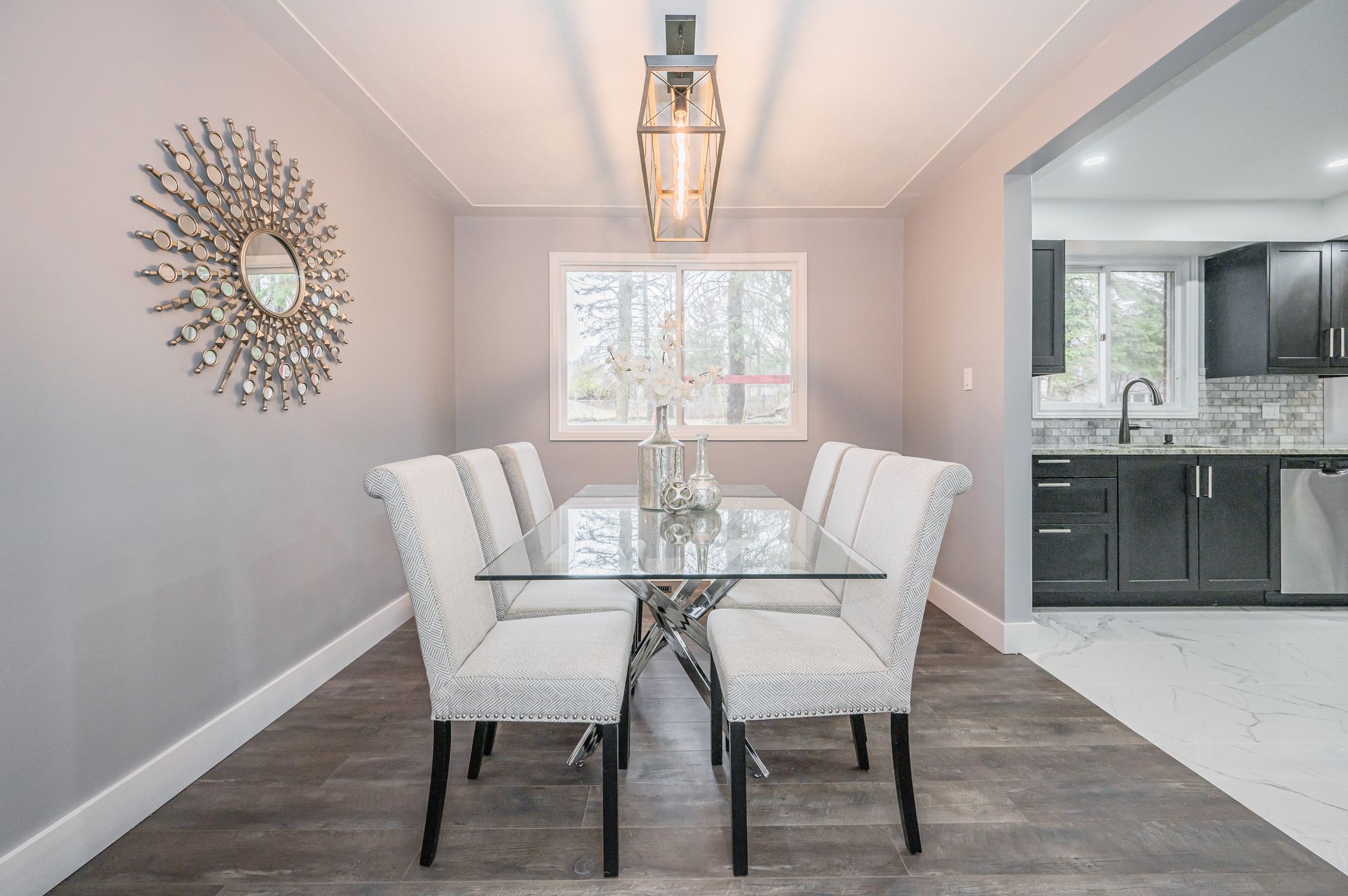 Dining room with a glass table and six white patterned chairs, gray walls, and a large mirror.