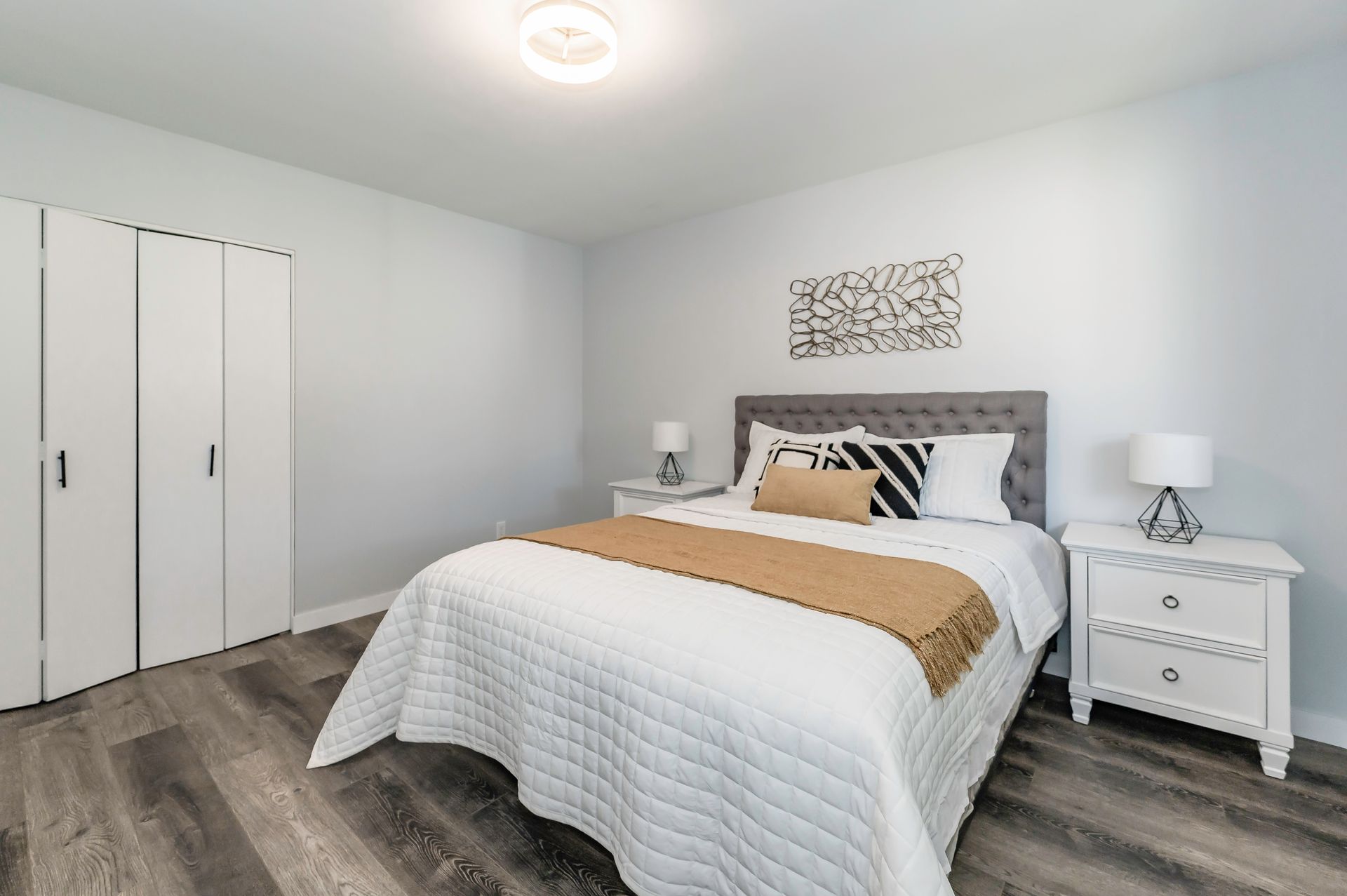 Bedroom with a bed, white bedding, nightstands, and a closet. Light gray walls and wood-look flooring.