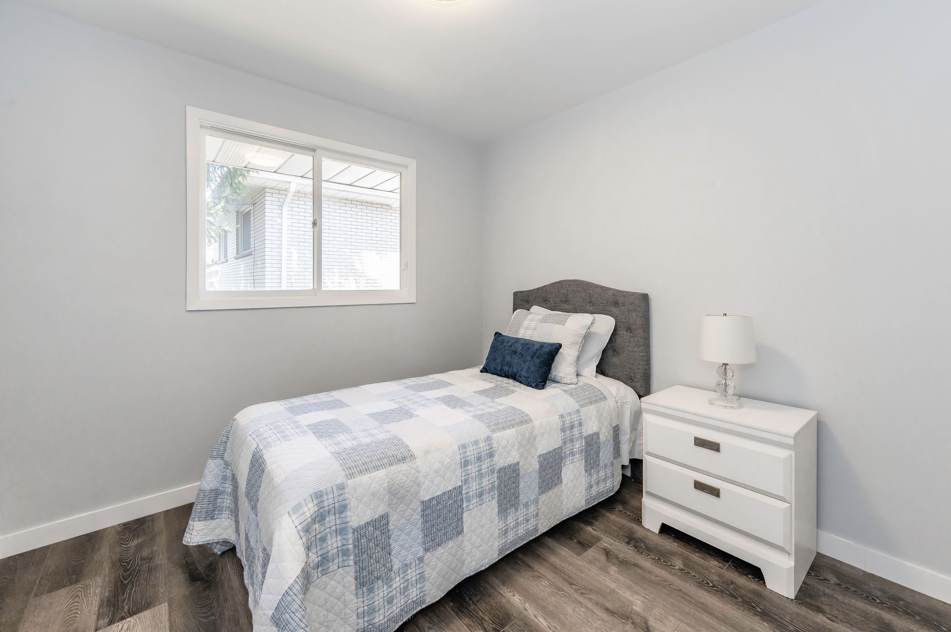 Bedroom with a twin bed, nightstand, and window. Gray walls and flooring.