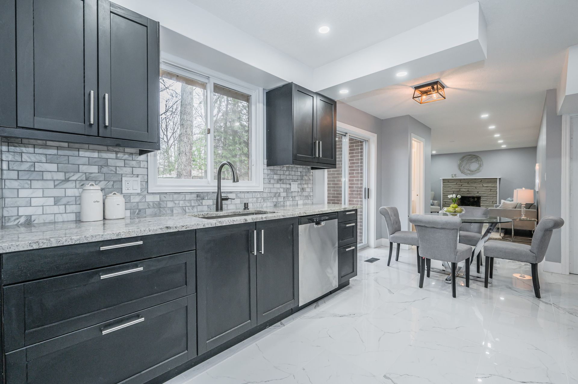 Dark kitchen with marble countertops, gray cabinets, and stainless steel appliances. Adjacent dining area with table and chairs.