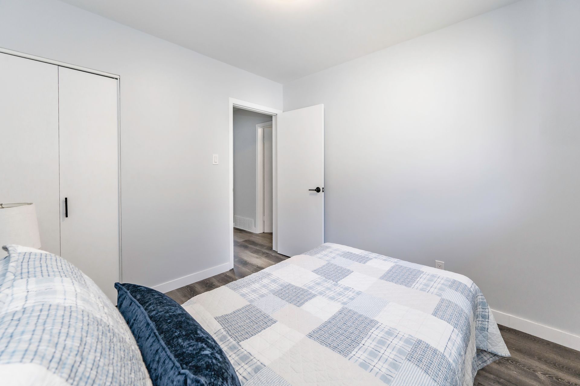 Bedroom with gray walls, white closet, and a blue and white patterned bedspread. A doorway leads to another room.