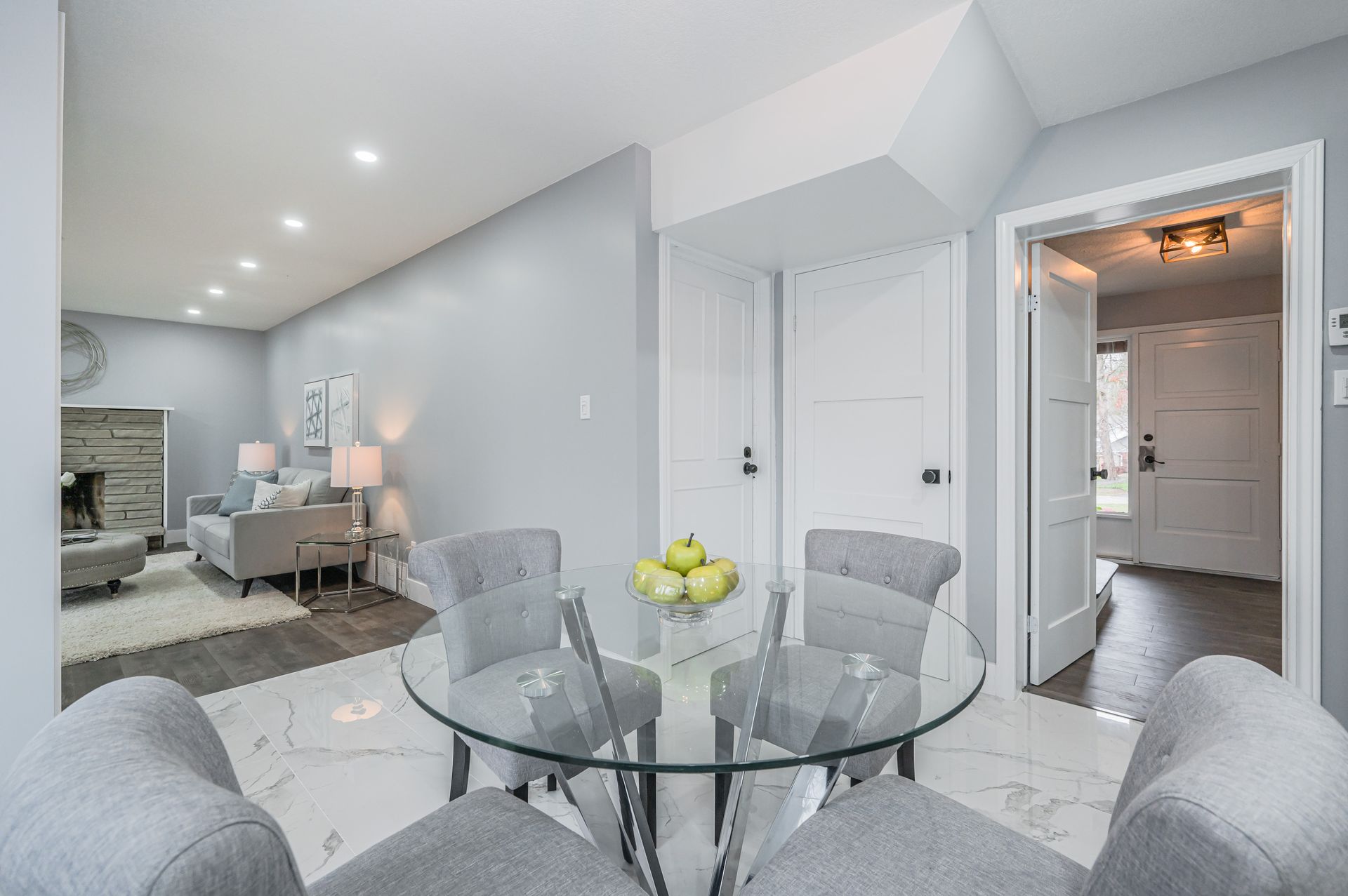 Dining room with glass table, gray chairs, and living room visible in background.
