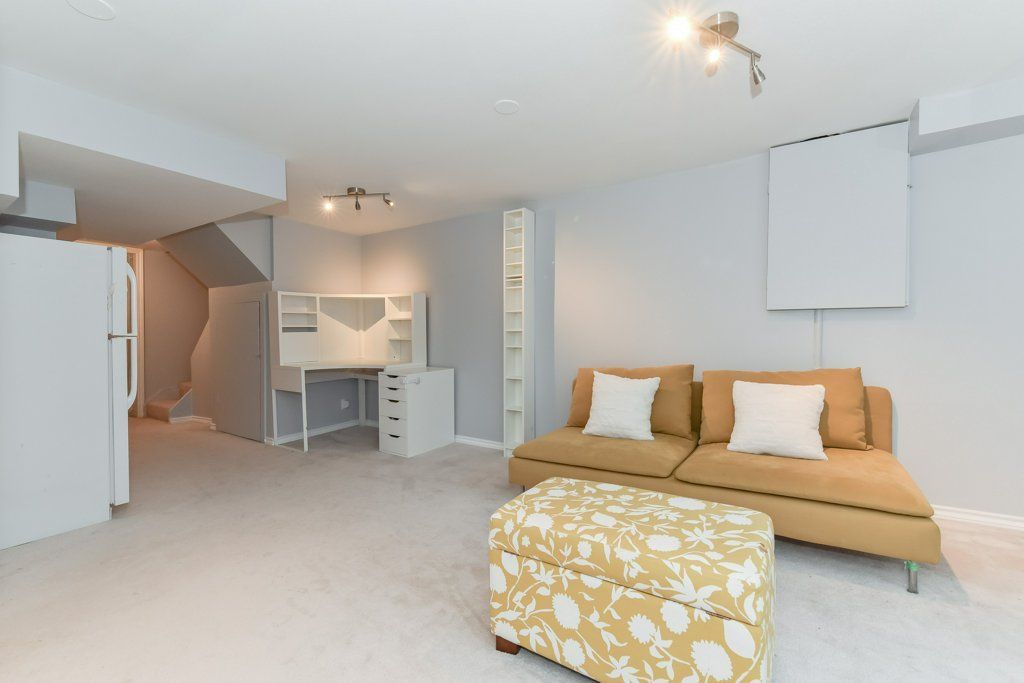 Cozy, modern basement with mustard-colored sofa, patterned ottoman, and built-in desk.
