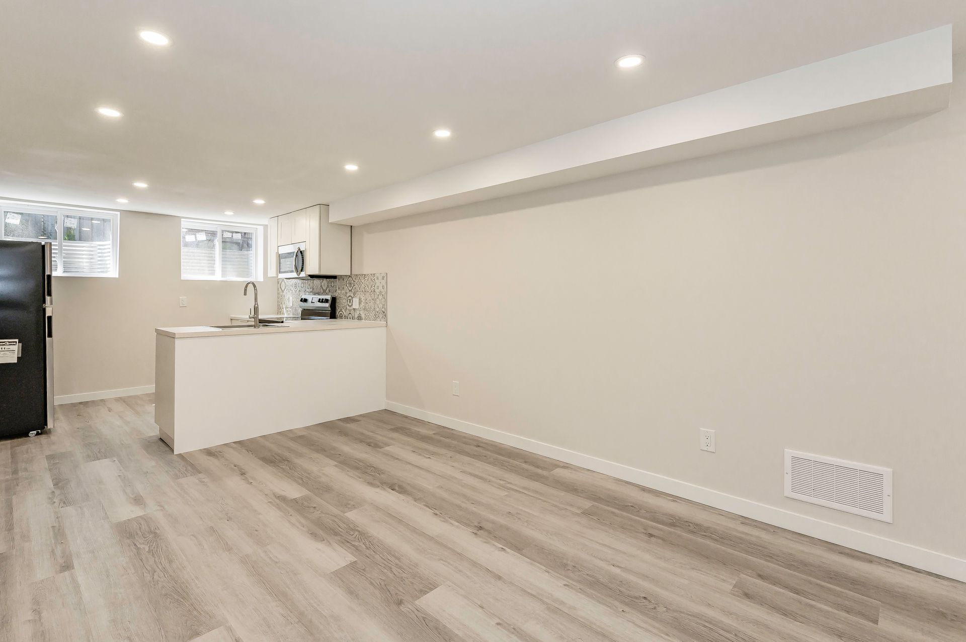 Bright, modern basement apartment with a small kitchen and light gray flooring.