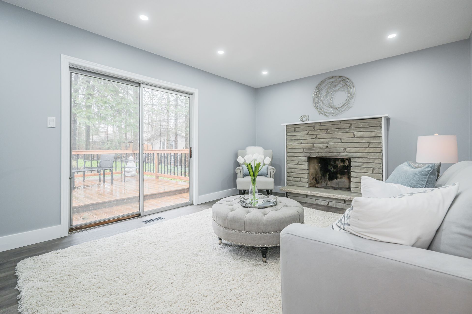 Living room with stone fireplace, sliding door to deck, gray walls, white rug, and furniture.
