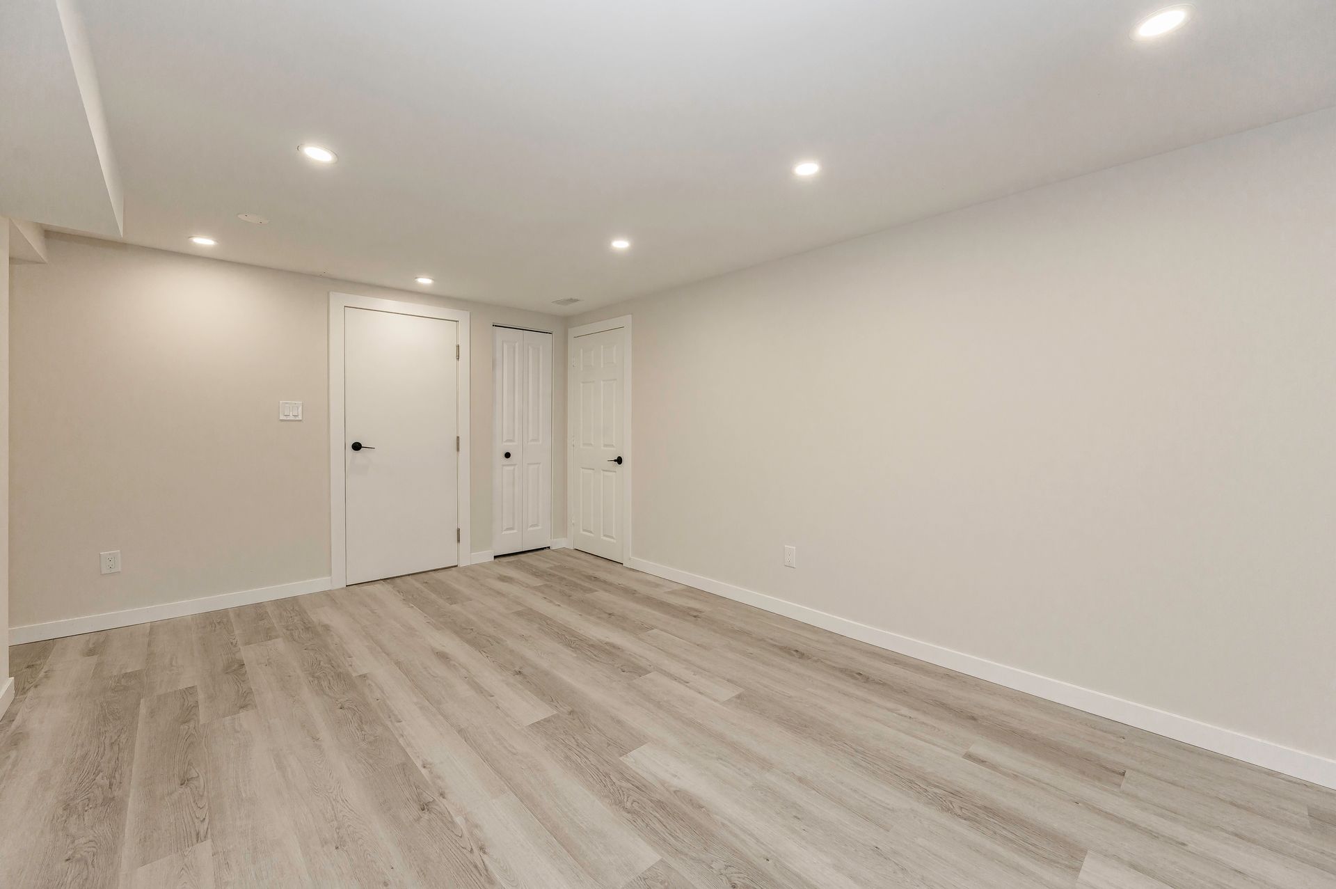 Empty room with light gray walls, white doors, and wood-look flooring.