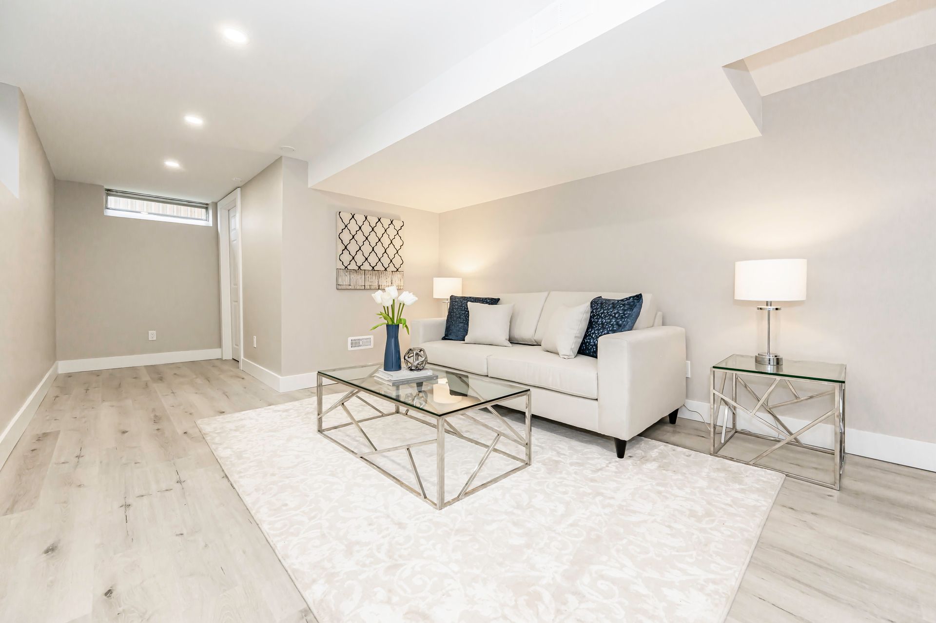 Basement living room with gray walls, white rug, light sofa, silver coffee table, and side table.
