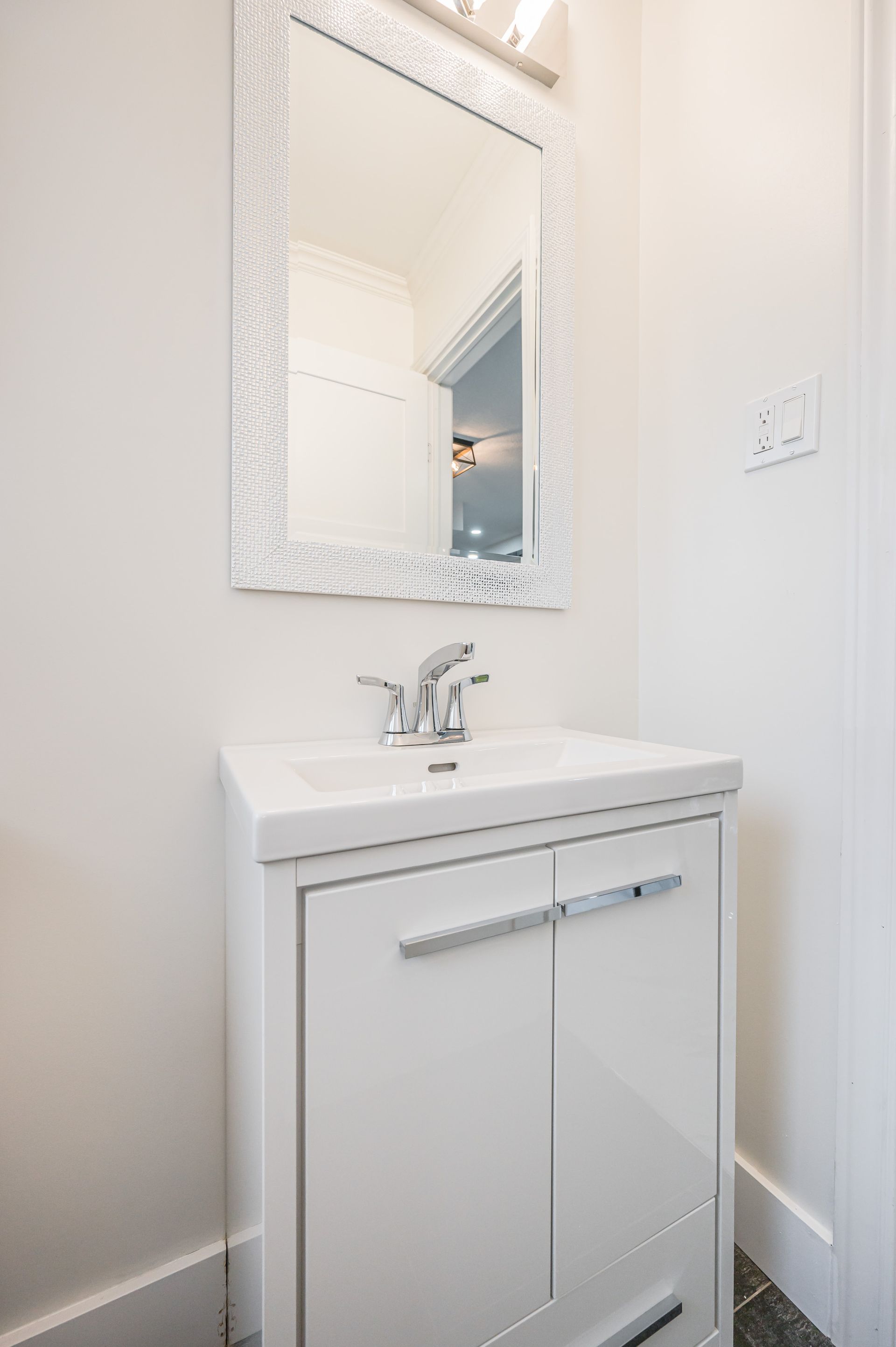 White bathroom vanity with sink and mirror, chrome faucet and handles.