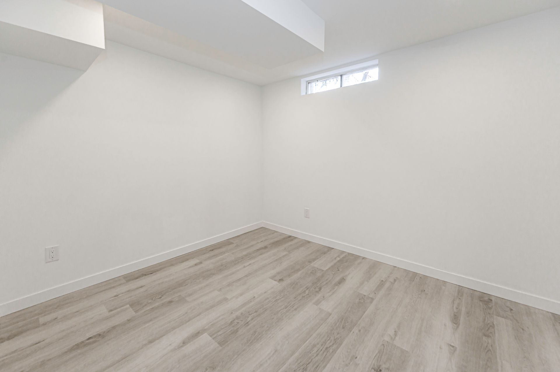 Empty room with gray wood-look flooring and white walls, featuring a small window.