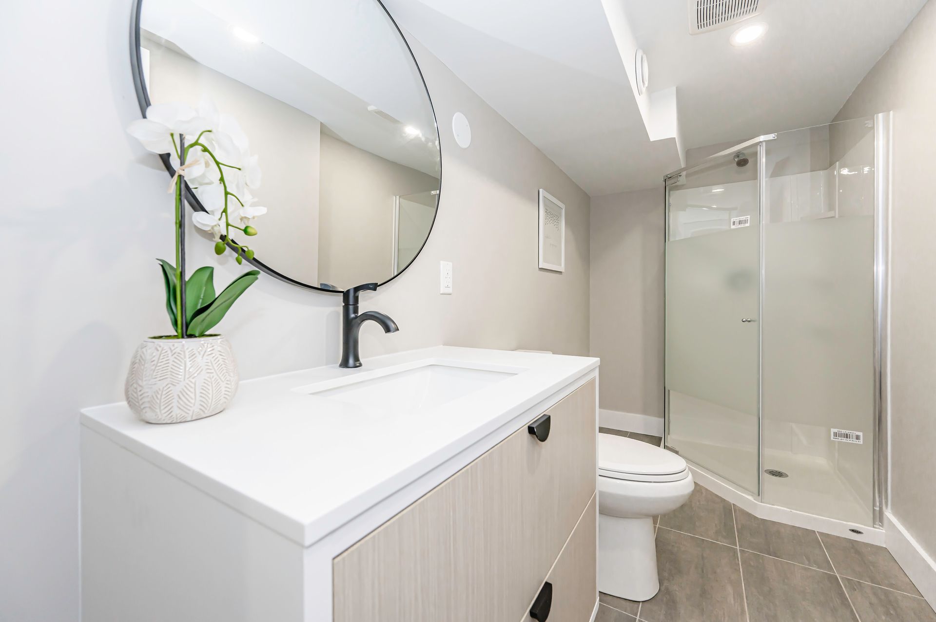 Bathroom with a white vanity, black faucet, round mirror, and glass shower.