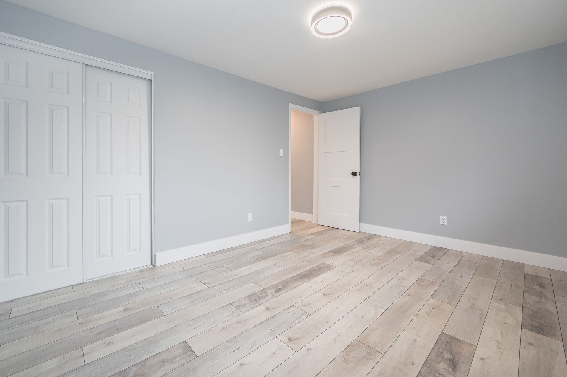 Empty bedroom with light blue walls, white doors, and light wood-look flooring.
