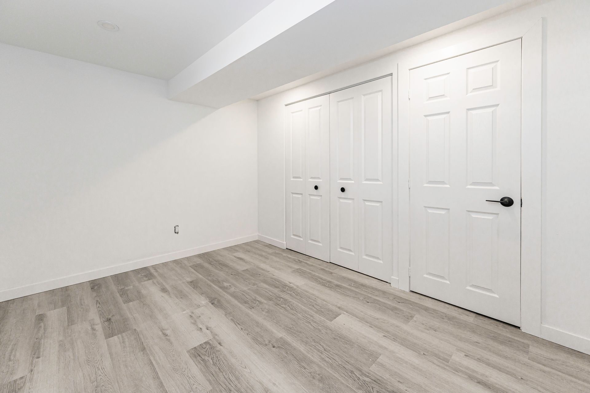 Empty white room with light wood-look floor, white doors and walls.