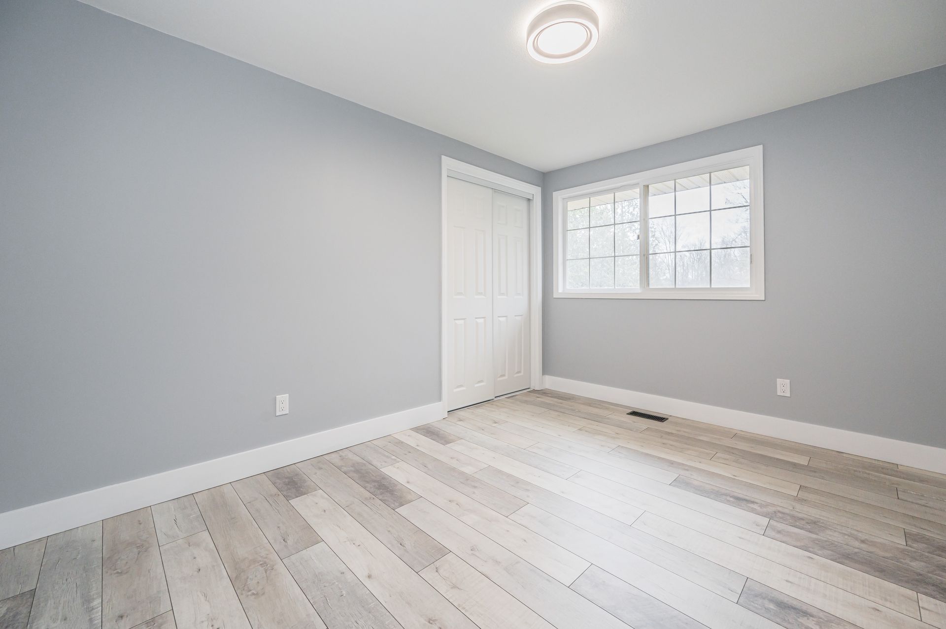 Empty bedroom with gray walls, white trim, and light wood-look flooring.