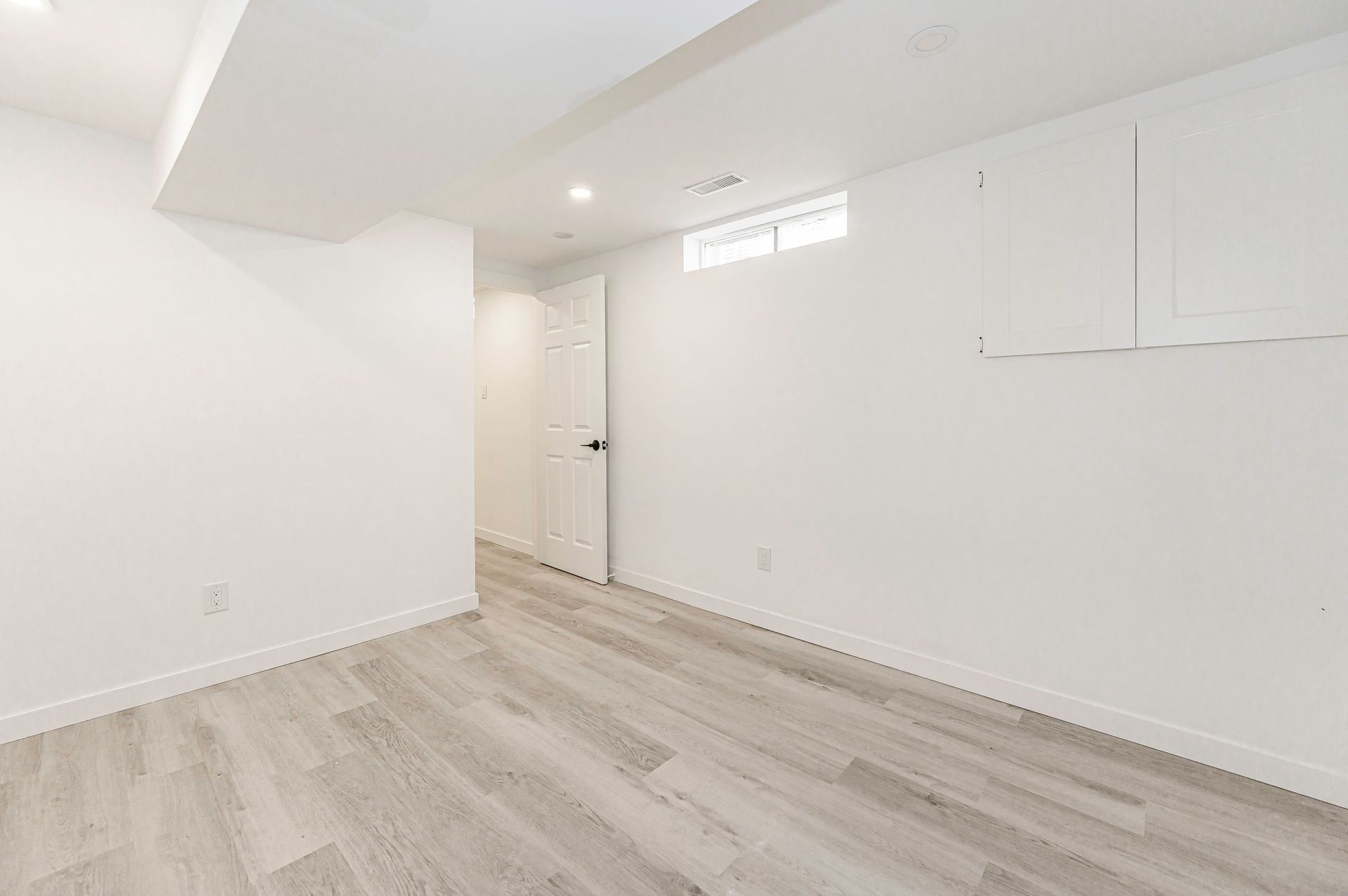 Empty white room with light gray flooring; door in the distance; window on the wall.