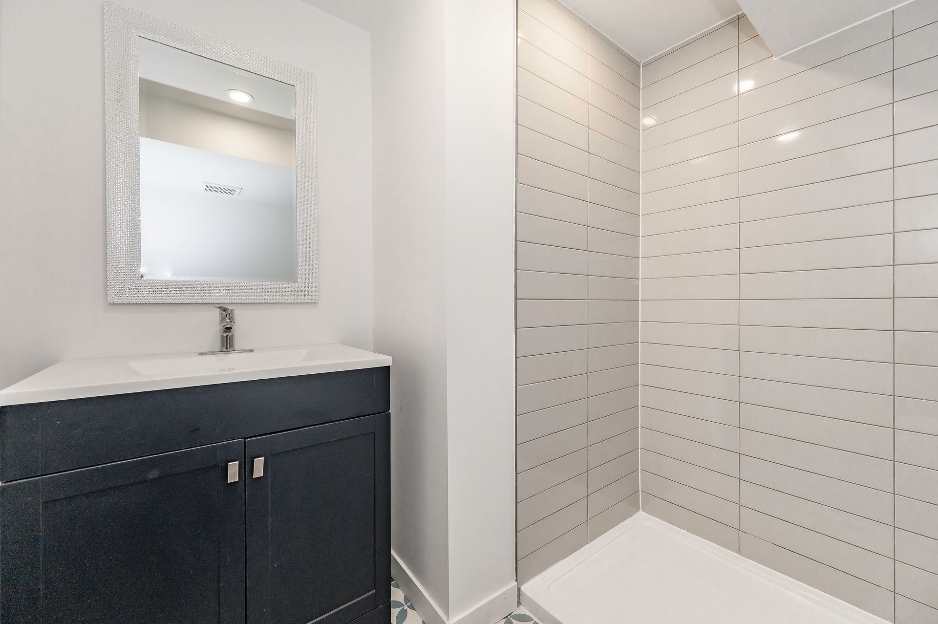 Modern bathroom with navy vanity, white countertop, framed mirror, and tiled shower.