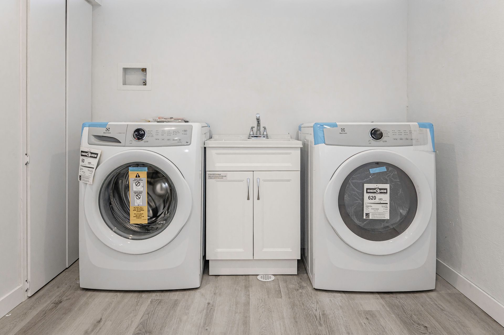 Laundry room with washing machines, sink, and cabinets. Light gray floor and white walls.