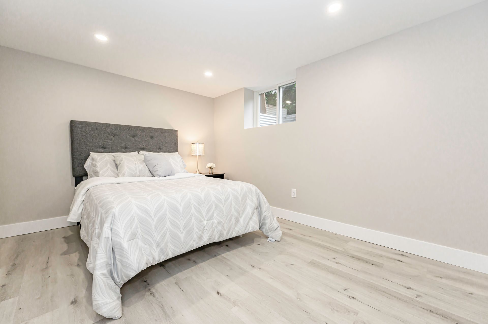 Bedroom with gray walls, light wood-look floor, bed with gray bedding and upholstered headboard.