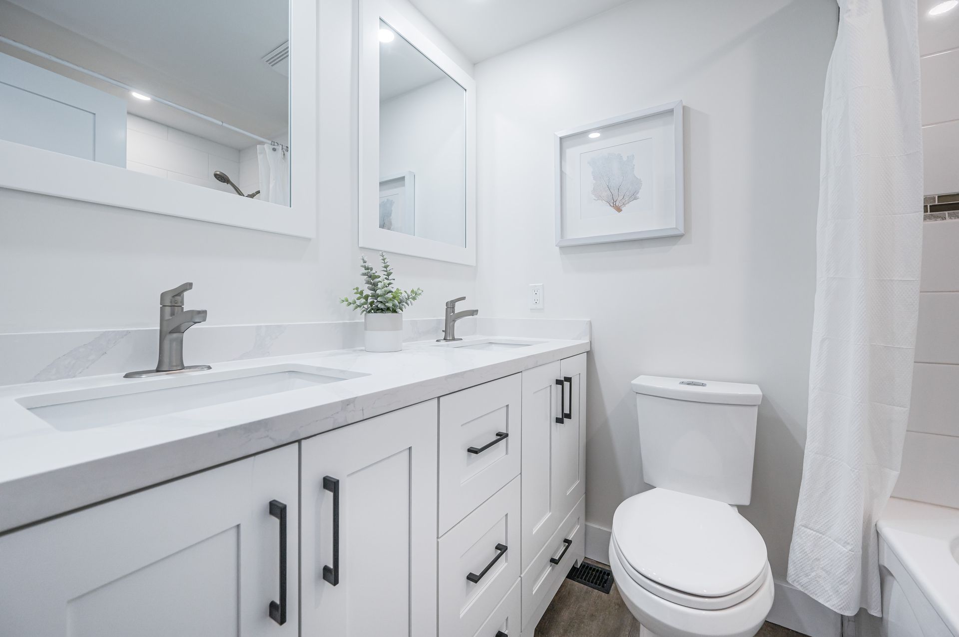 White bathroom with double vanity, toilet, and framed art.