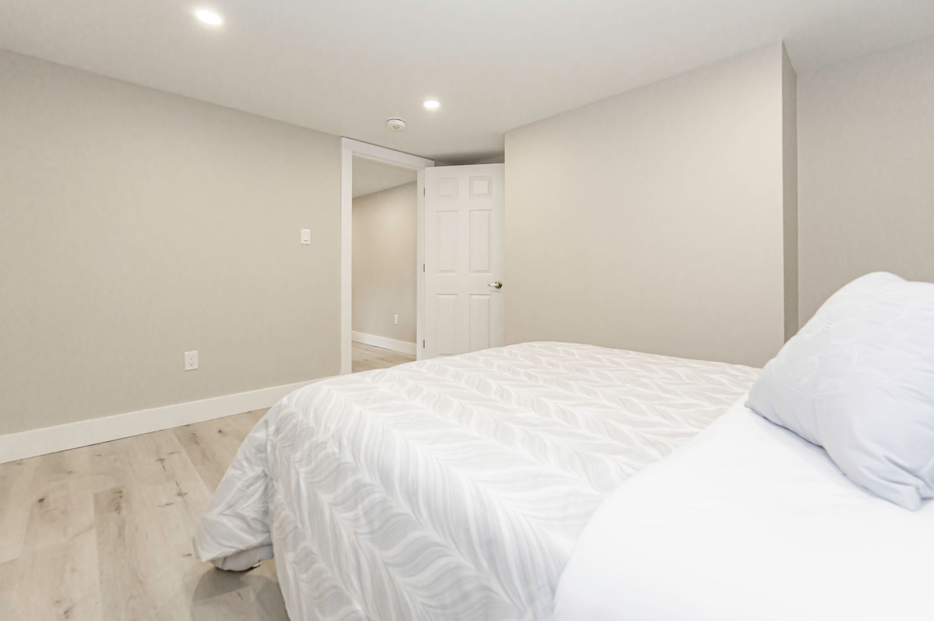 Bedroom with a bed, light gray walls, and a door leading to another room.