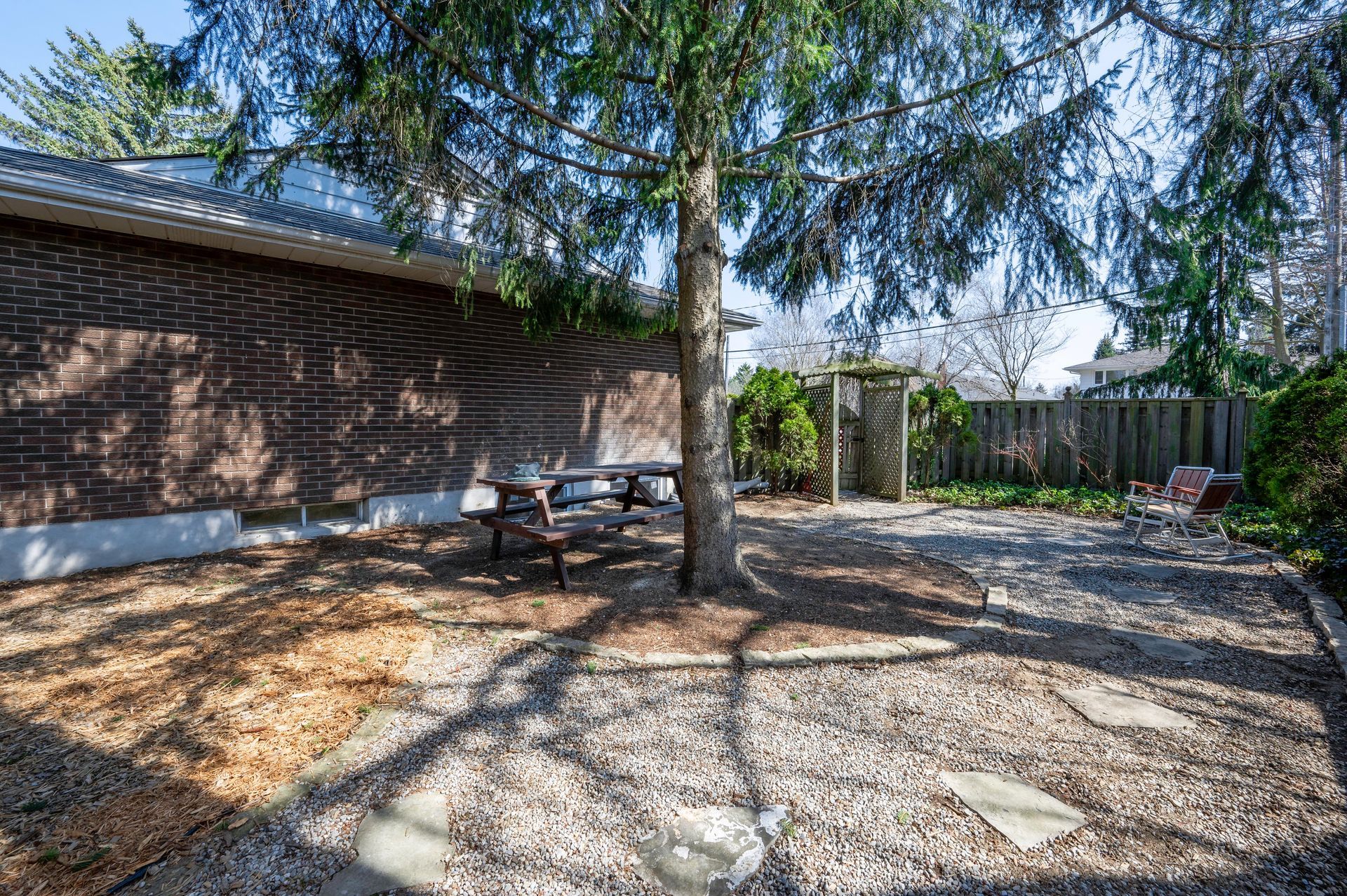 Backyard with a gravel ground, tree, and a wooden picnic table next to a brick building.