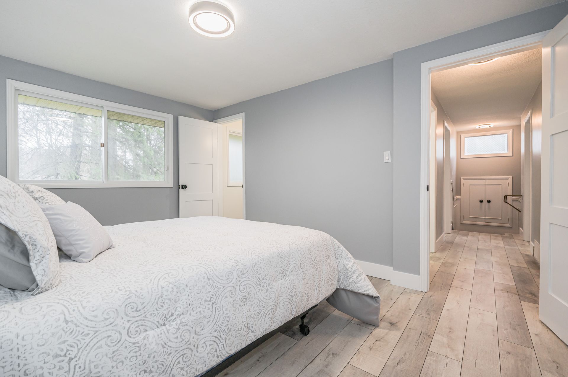 Bedroom with a bed, a window, a doorway to a hallway, and light gray walls.
