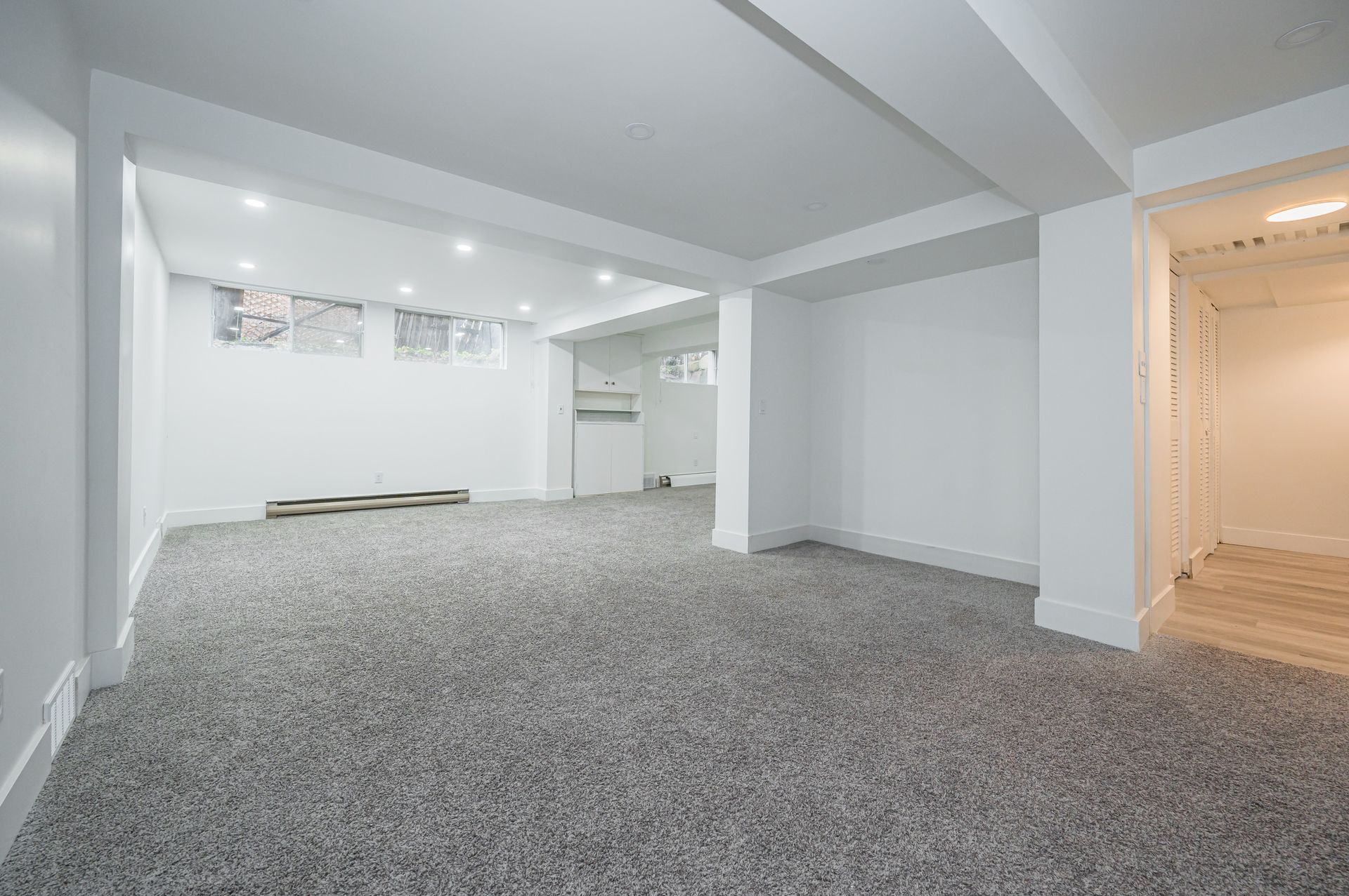 Empty, carpeted basement room painted white. Recessed ceiling lights.