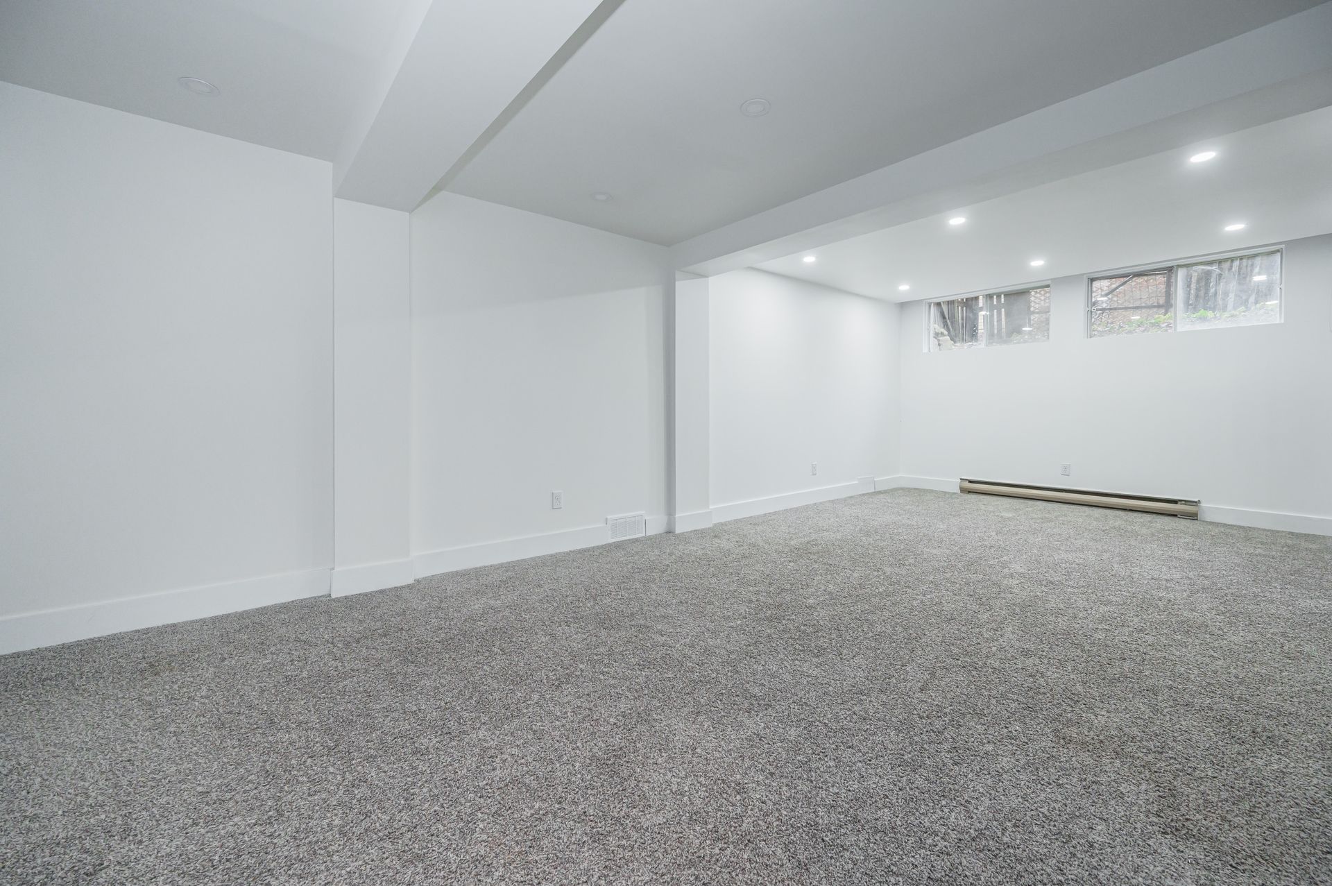 Empty white-walled room with gray carpet flooring and small windows near the ceiling.
