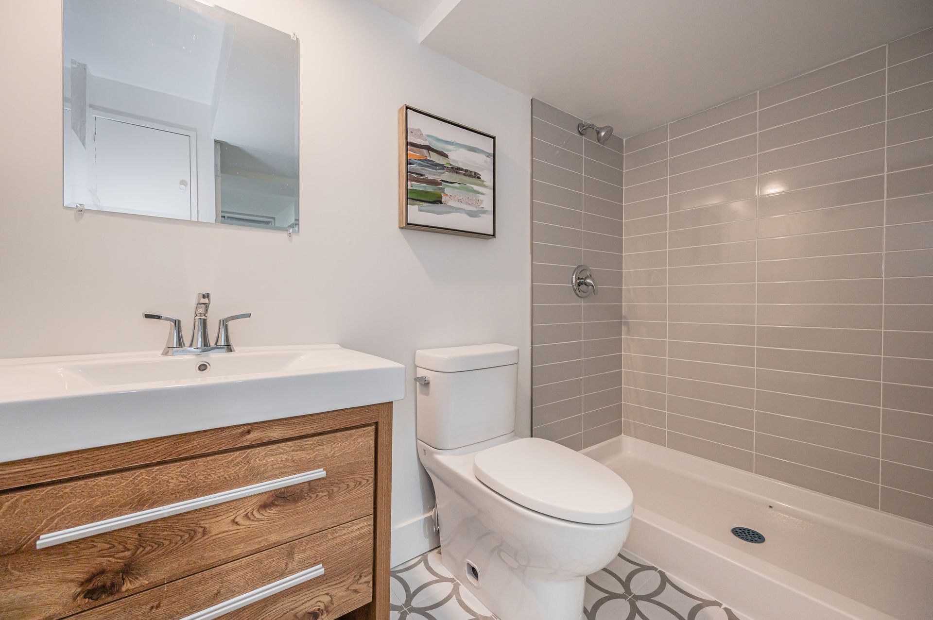 Bathroom with a wooden vanity, white toilet, gray tiled shower, and a decorative rug.