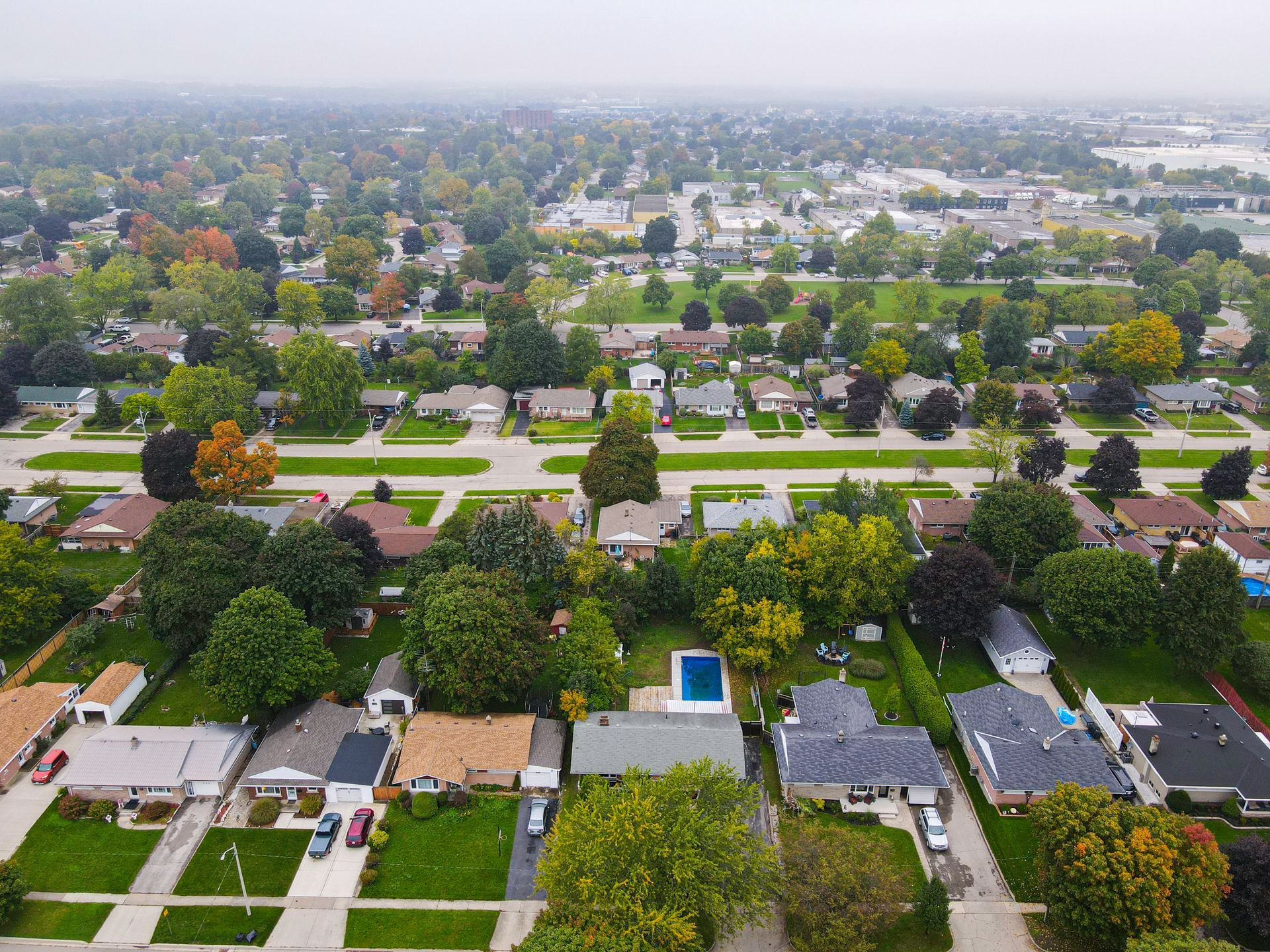 Aerial view of a suburban neighborhood with houses, trees, streets, and a swimming pool.