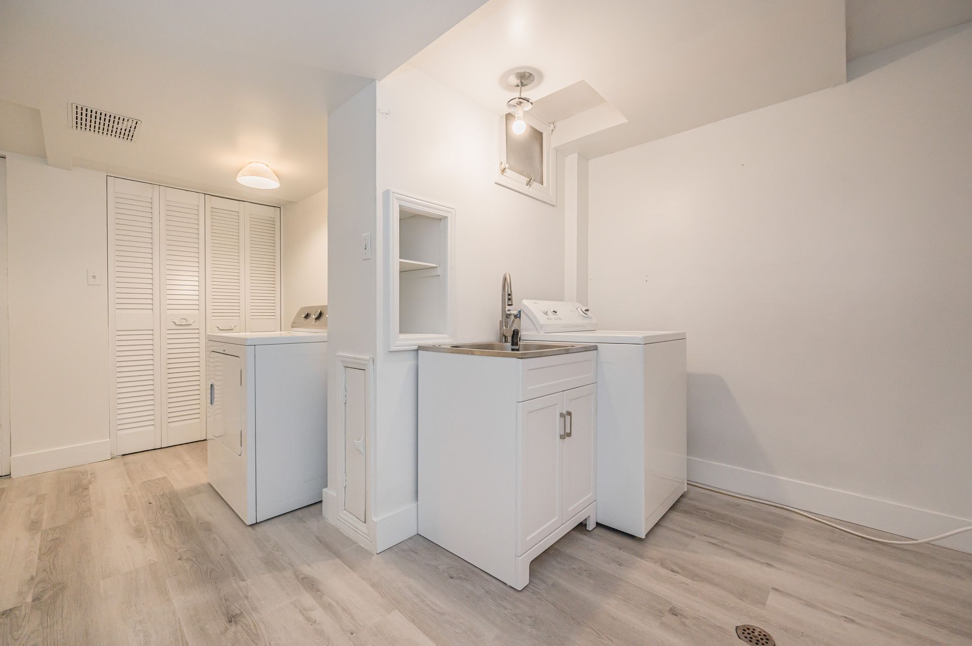 White laundry room with washer, dryer, sink, cabinets, and folding doors.