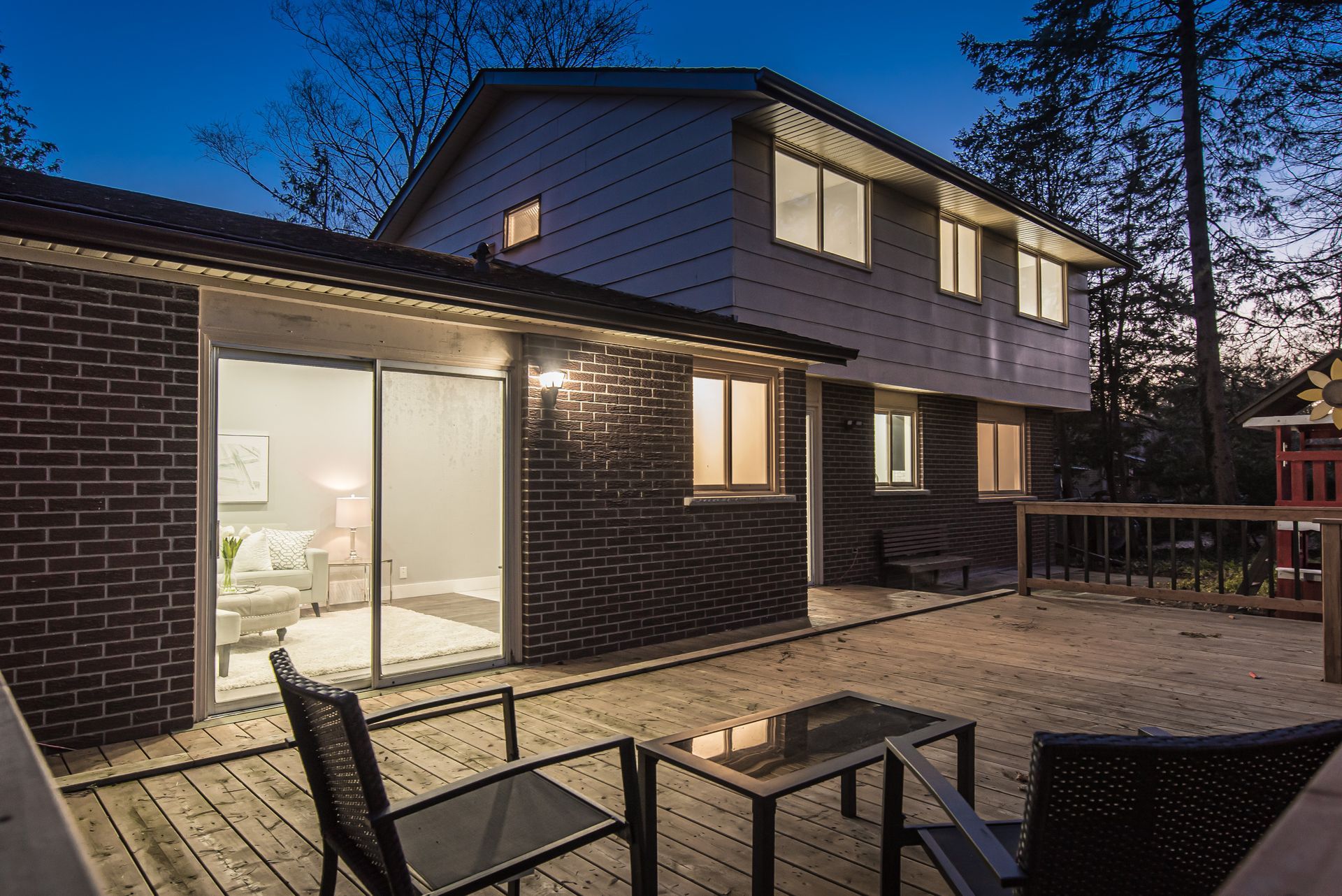 Backyard view of a two-story home with a deck. The brick siding contrasts the siding of the second level.