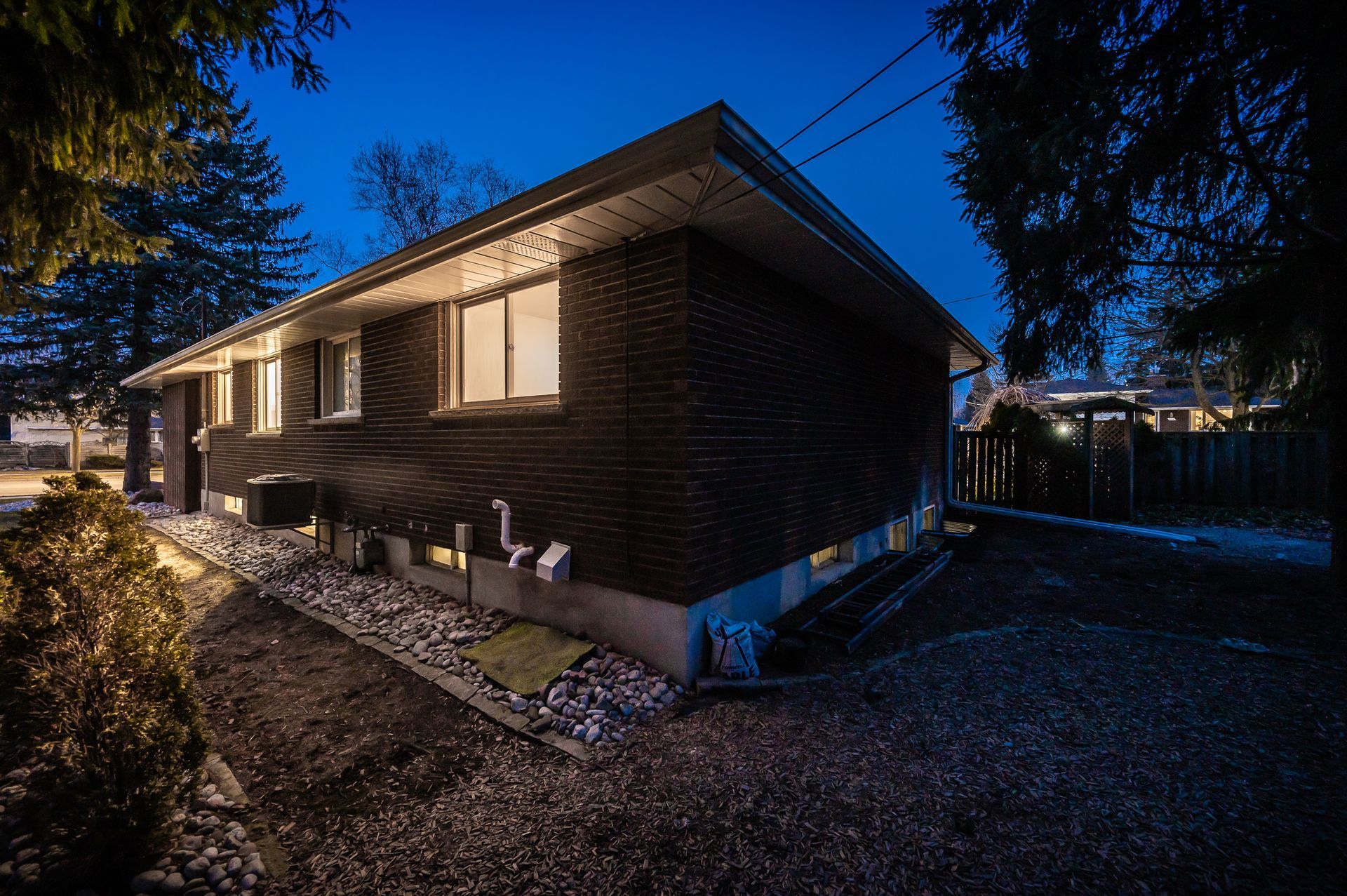 Dark brick house exterior at dusk with lit windows and gravel landscaping.