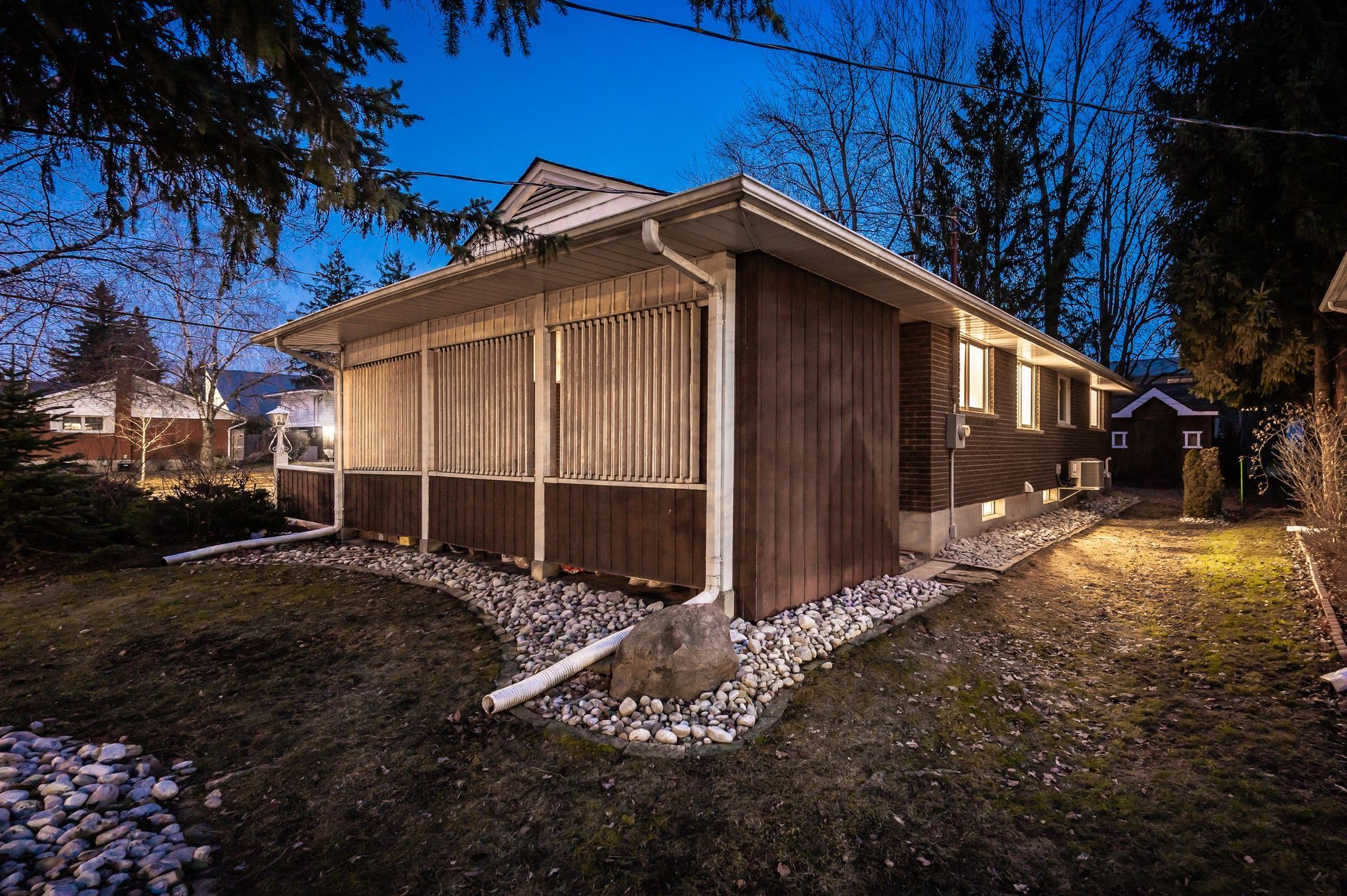 Exterior of a brown house at dusk, with a porch and surrounding yard.