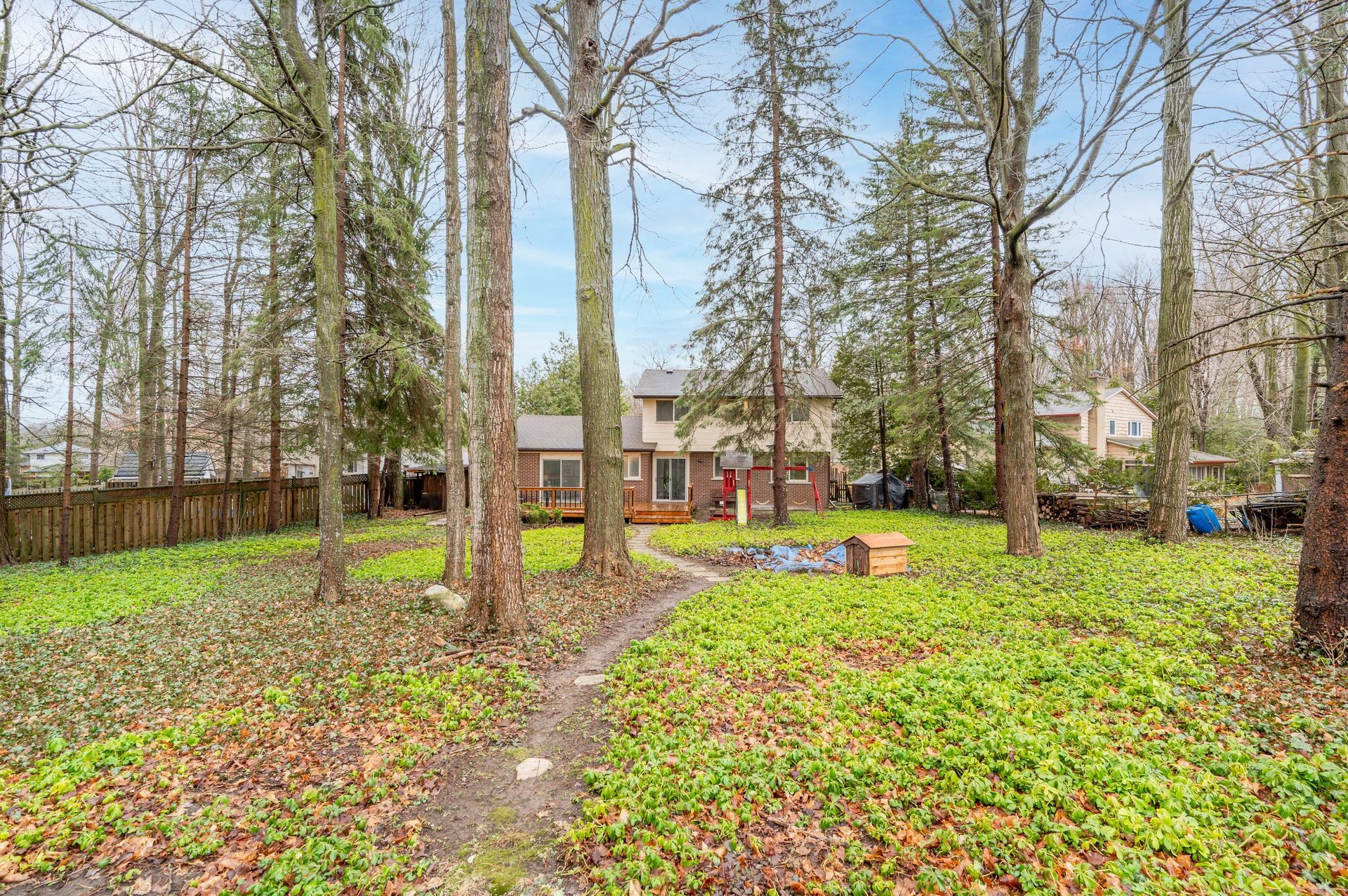 Backyard view of a house surrounded by trees and greenery with a path leading to a deck.