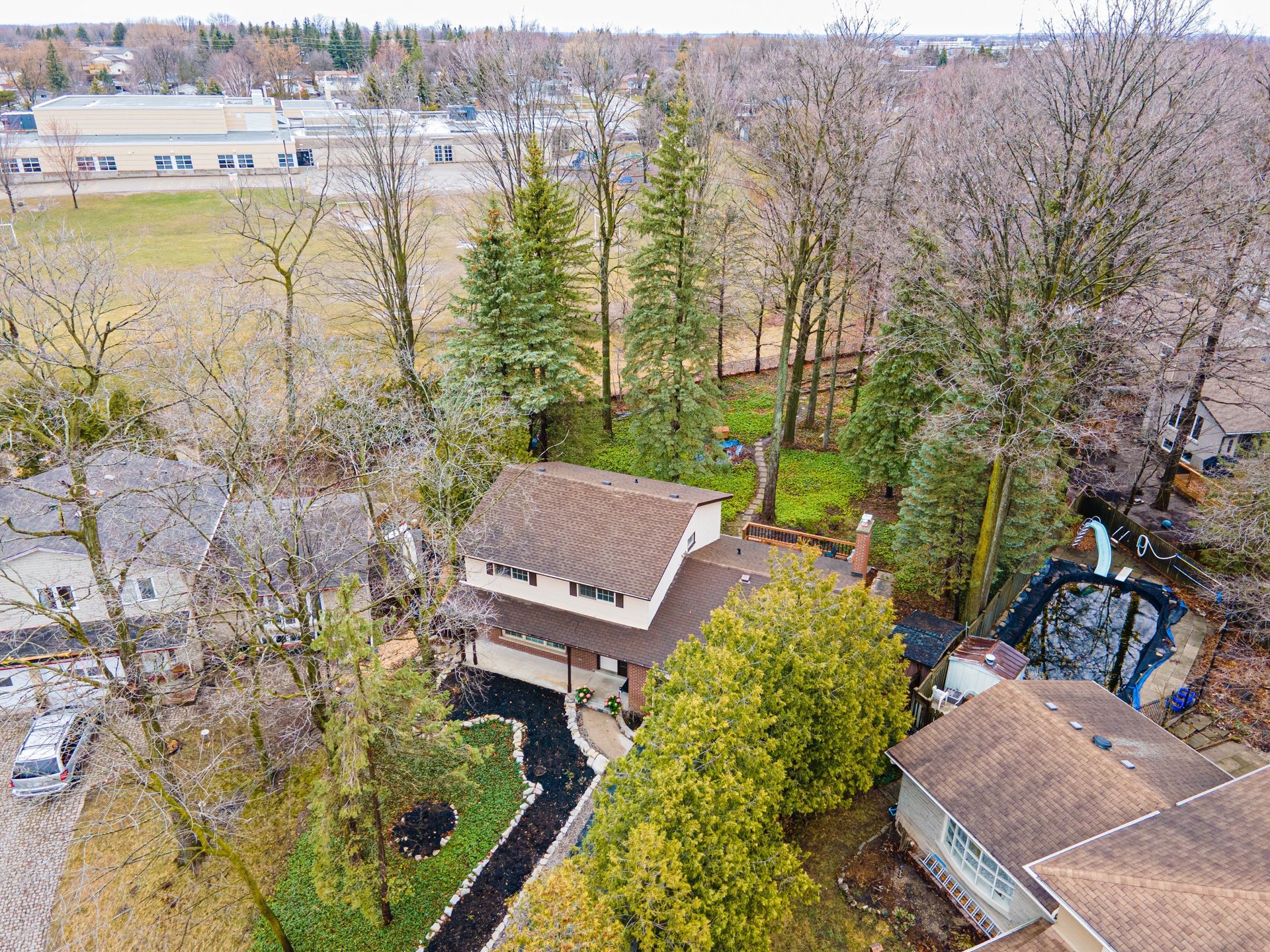 Aerial view of a two-story house with a brown roof and a black walkway; a school is in the background.