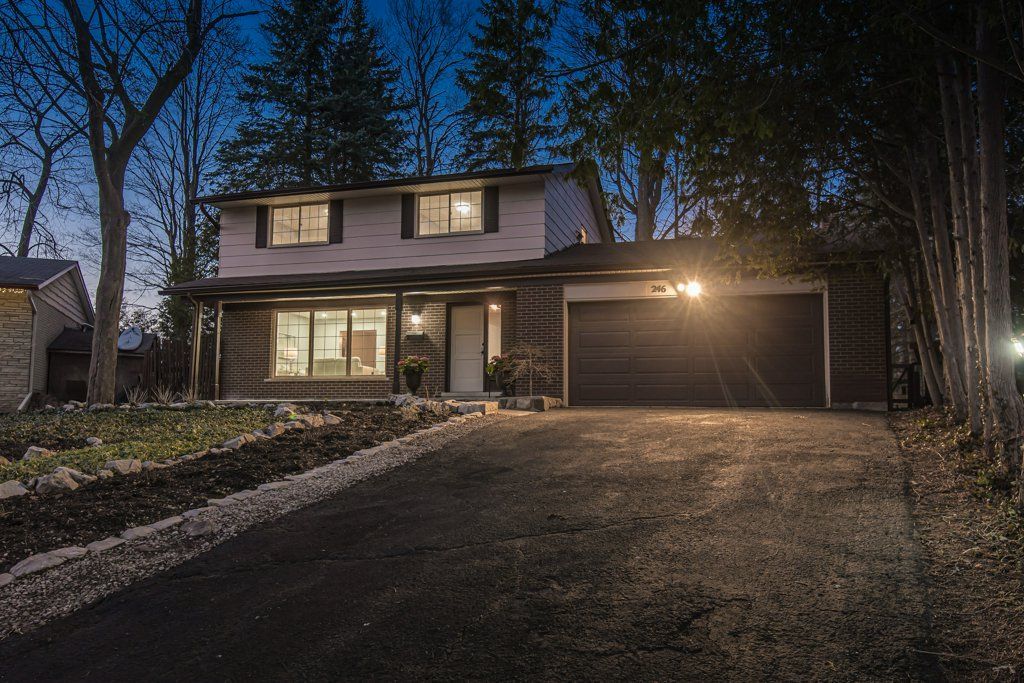 Two-story house at dusk, with a dark driveway, lit garage, and trees in the background.