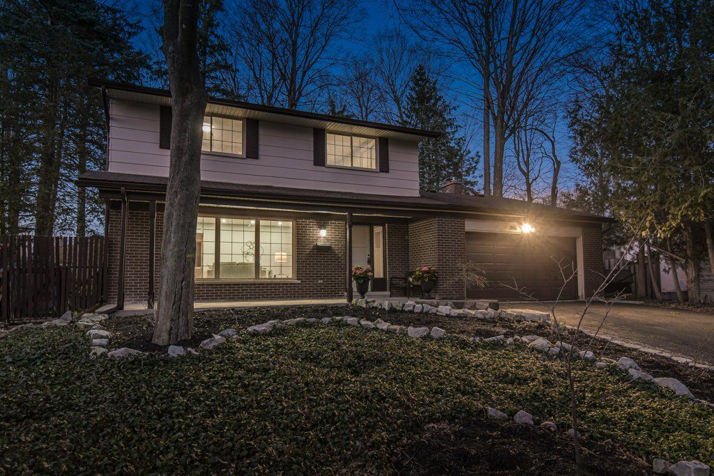 Two-story house at dusk, lit interior, covered entrance, driveway, surrounded by trees and landscaping.