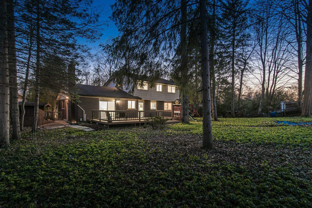 Two-story house with lights on, viewed from a wooded yard at dusk.