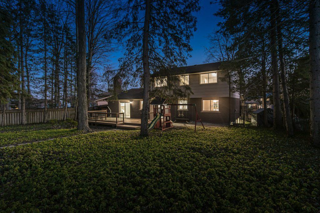 House exterior at night, lit windows, backyard with trees and grass, dark blue sky.
