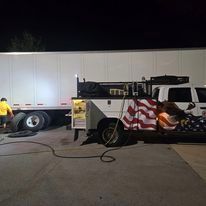 A tow truck with an american flag painted on the side is parked next to a semi truck.