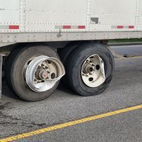 A semi truck with a broken rim is parked on the side of the road.