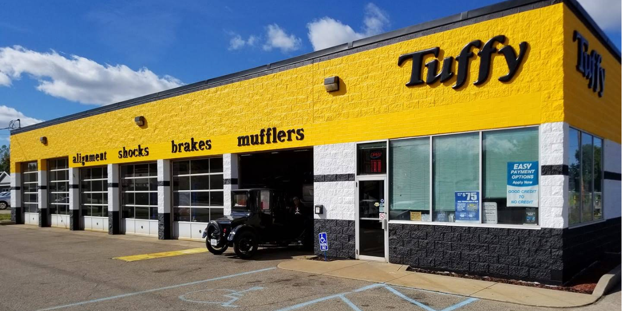 A yellow Tuffy auto repair shop with black lettering and an old car in one bay.