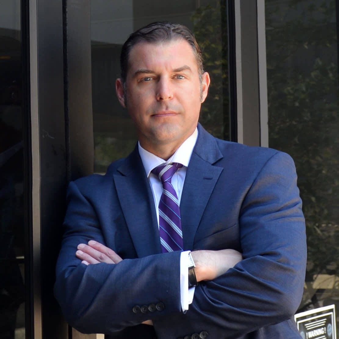 A man in a suit and tie is standing with his arms crossed