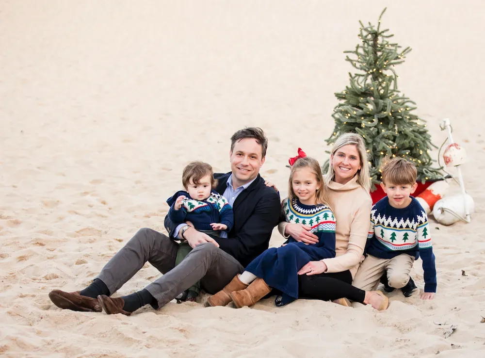 A family is sitting on the sand in front of a christmas tree.