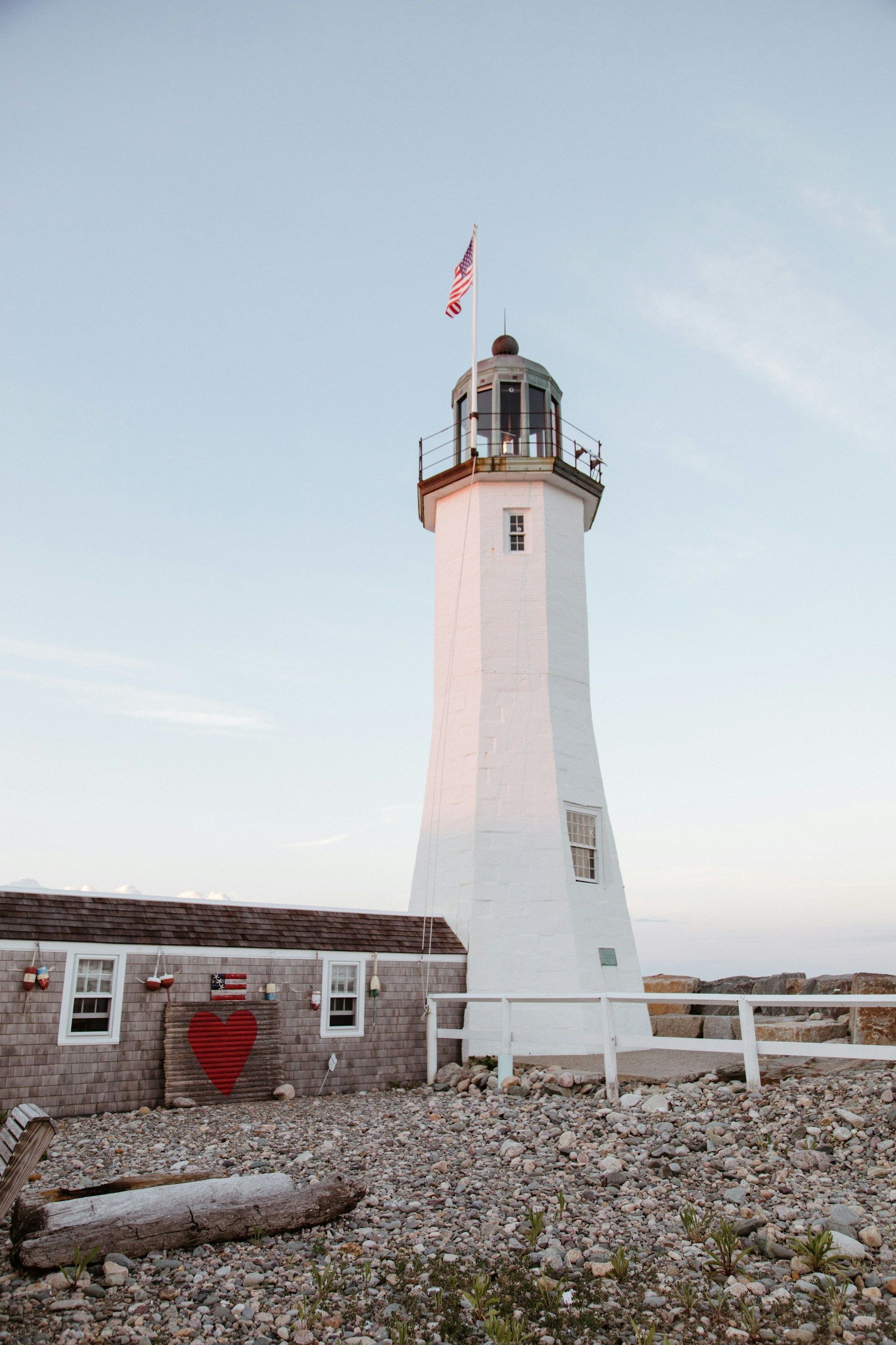 A white lighthouse is sitting on top of a rocky beach next to a house.