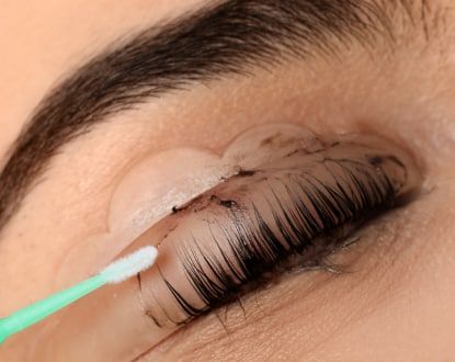 A woman is cleaning her eyelashes with a cotton swab.