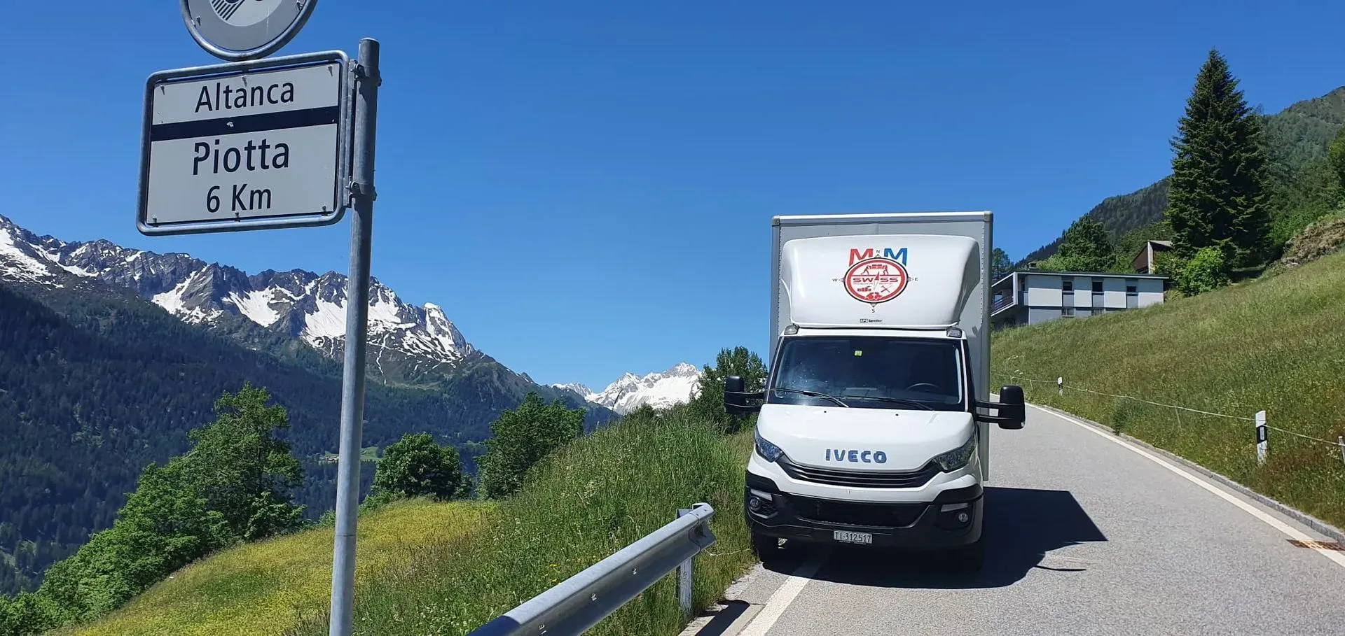 Un furgone bianco percorre una strada con le montagne sullo sfondo.